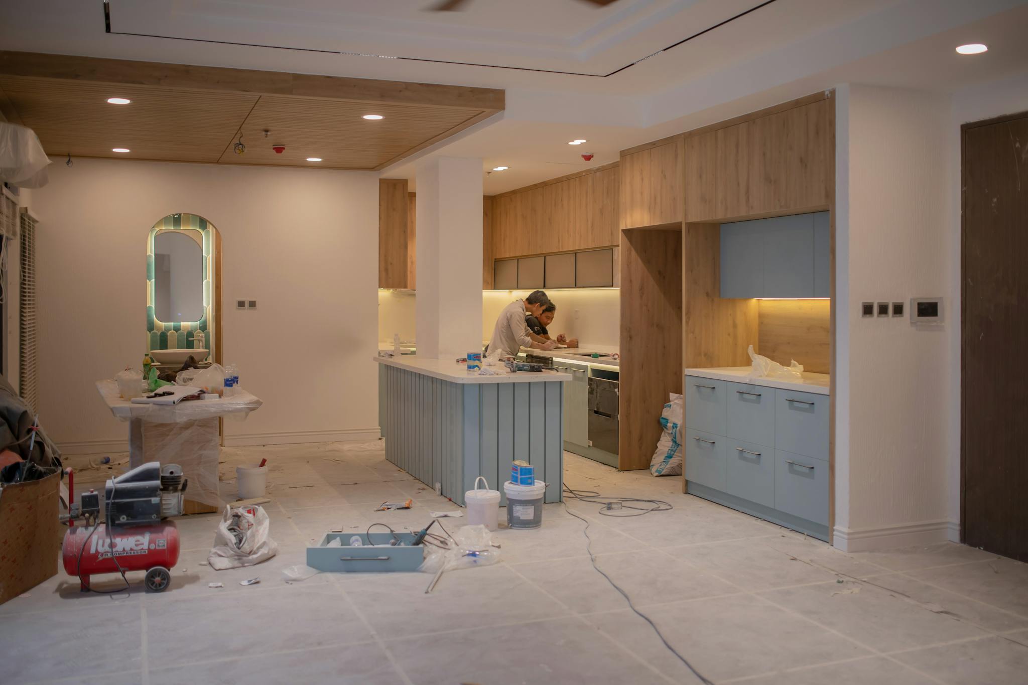 Gallery A modern kitchen undergoing renovation, featuring a worker, tools, and materials.