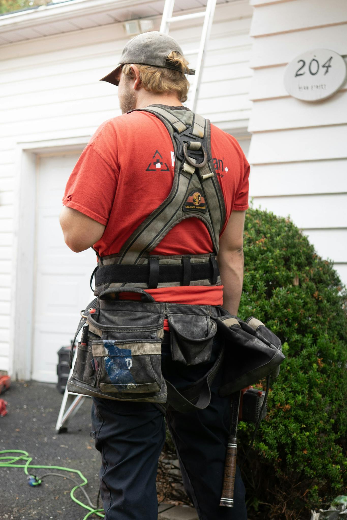 Gallery Back view of construction worker in red shirt and safety harness next to a house.